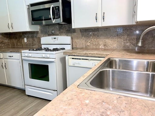 kitchen featuring decorative backsplash, white cabinetry, a sink, wood finished floors, and white appliances