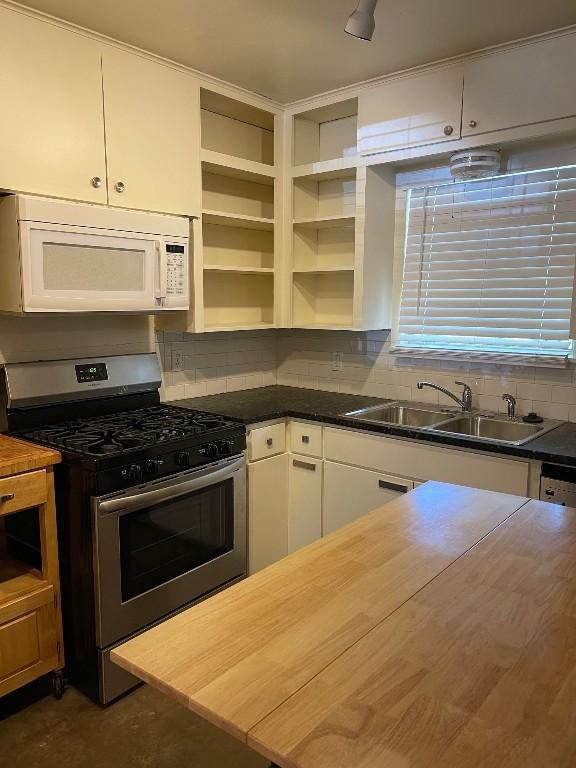 kitchen with stainless steel range with gas cooktop, tasteful backsplash, white microwave, white cabinets, and a sink