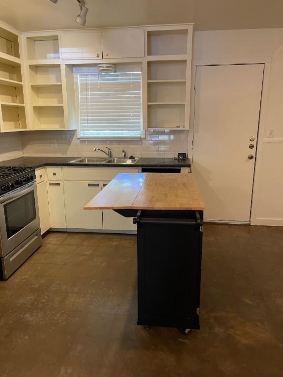 kitchen featuring stainless steel gas range, a sink, decorative backsplash, and open shelves