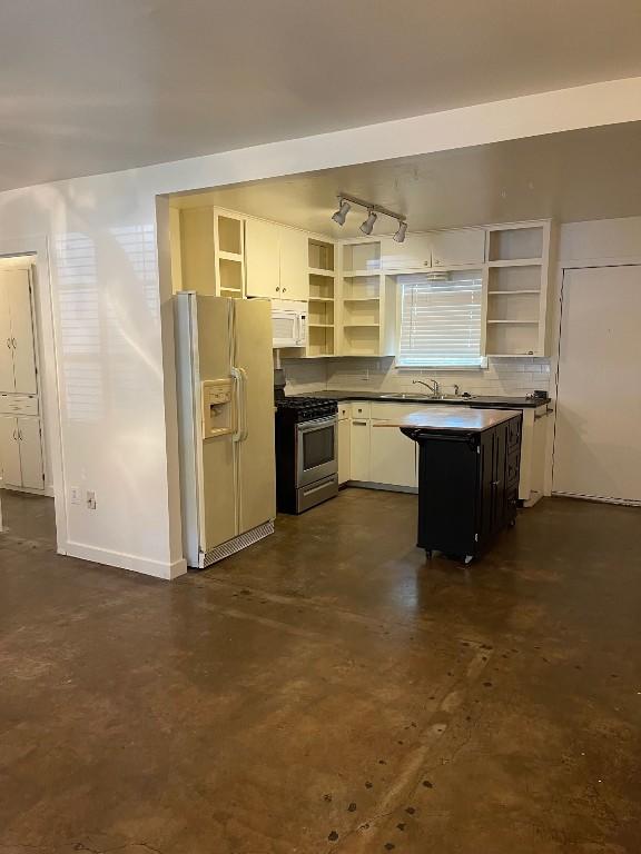 kitchen featuring open shelves, dark countertops, a sink, white appliances, and concrete floors