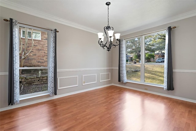 unfurnished dining area featuring a notable chandelier, crown molding, and wood finished floors