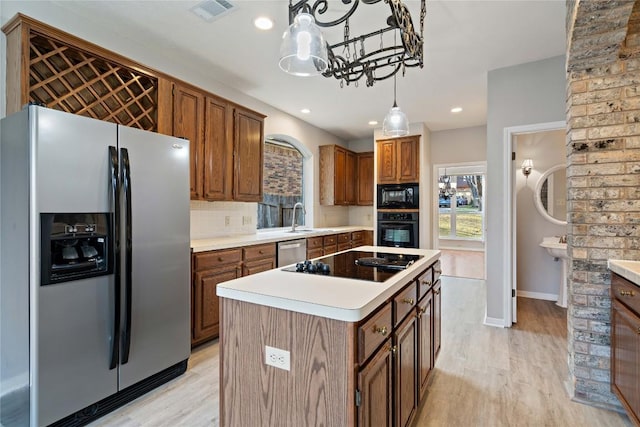 kitchen with tasteful backsplash, visible vents, a center island, light wood-type flooring, and black appliances