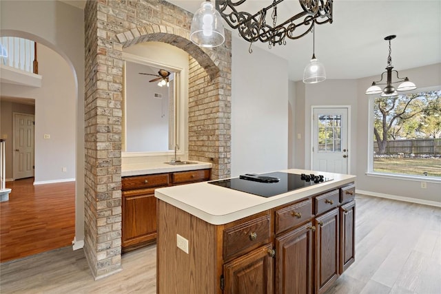 kitchen featuring arched walkways, a sink, light wood-style flooring, and black electric stovetop