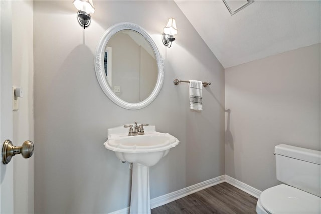 half bathroom with baseboards, vaulted ceiling, toilet, and wood finished floors