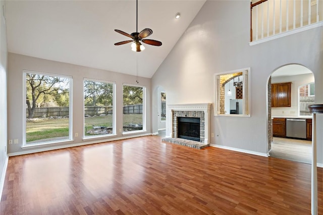 unfurnished living room featuring arched walkways, baseboards, ceiling fan, light wood-type flooring, and a brick fireplace