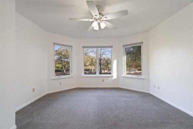 empty room featuring baseboards, dark carpet, and a ceiling fan