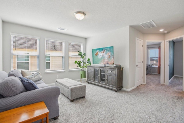 living area with baseboards, light colored carpet, visible vents, and a healthy amount of sunlight