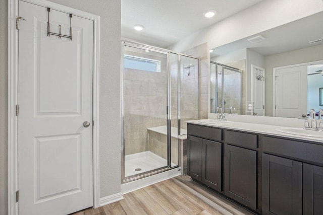 bathroom with a sink, wood finished floors, a stall shower, and double vanity