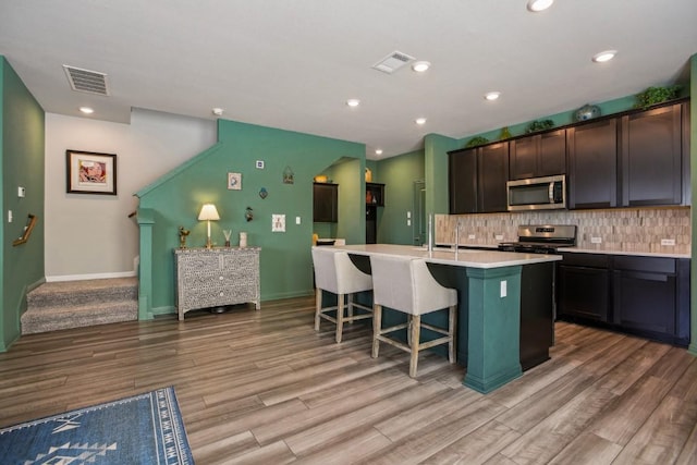 kitchen featuring a kitchen island with sink, backsplash, visible vents, and appliances with stainless steel finishes