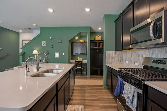 kitchen featuring wood finished floors, a sink, stainless steel appliances, light countertops, and backsplash