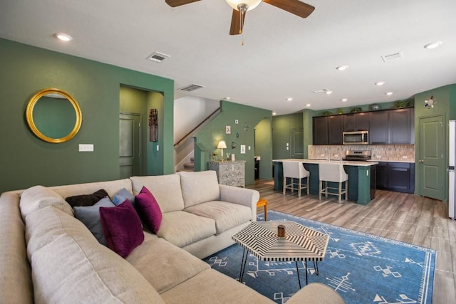 living room featuring ceiling fan, stairway, visible vents, and light wood-style flooring