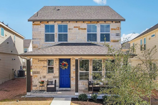 view of front facade with a porch, stone siding, cooling unit, and roof with shingles