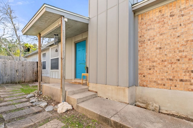 property entrance featuring fence, board and batten siding, and brick siding