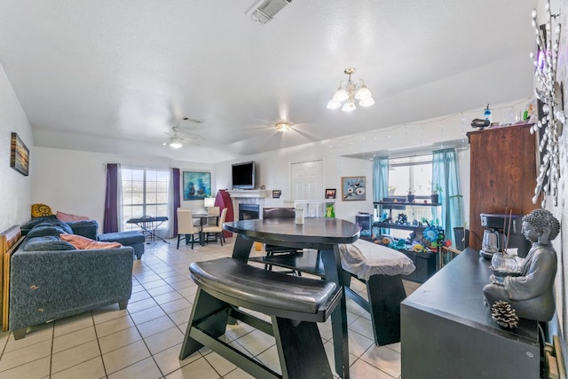 dining space featuring ceiling fan with notable chandelier, light tile patterned flooring, a fireplace, and visible vents