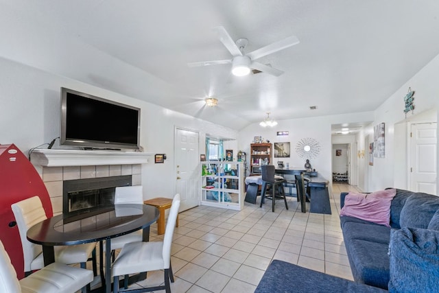 living room with ceiling fan with notable chandelier, vaulted ceiling, a tiled fireplace, and light tile patterned floors