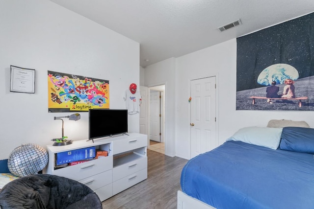 bedroom with visible vents, a textured ceiling, and wood finished floors