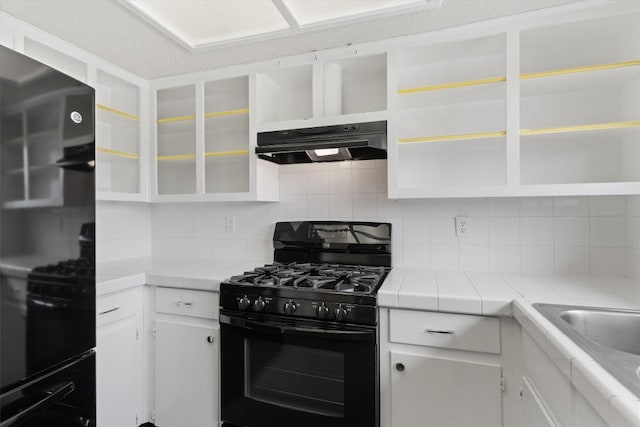 kitchen with range, black gas stove, under cabinet range hood, open shelves, and backsplash