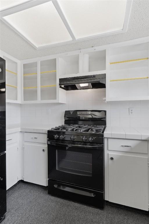 kitchen featuring black gas range, under cabinet range hood, white cabinetry, backsplash, and open shelves