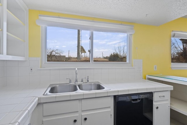 kitchen featuring a textured ceiling, a sink, white cabinets, black dishwasher, and decorative backsplash