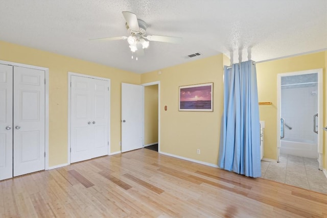 unfurnished bedroom featuring multiple closets, visible vents, ensuite bathroom, a textured ceiling, and wood finished floors