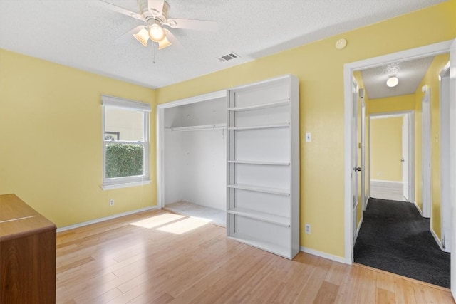 unfurnished bedroom with a closet, visible vents, a textured ceiling, wood finished floors, and baseboards