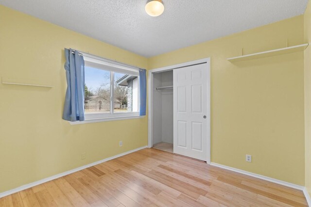 unfurnished bedroom with a textured ceiling, a closet, baseboards, and wood finished floors