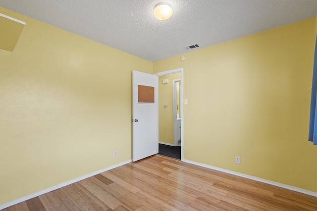 unfurnished room with light wood-type flooring, visible vents, baseboards, and a textured ceiling