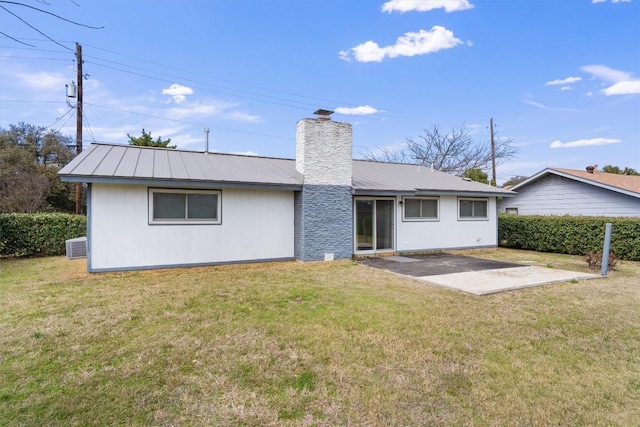 back of house with a chimney, metal roof, a lawn, and a patio area