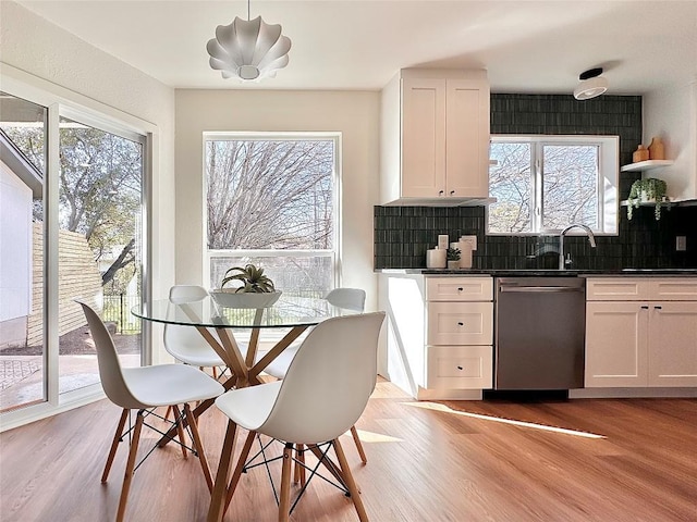 kitchen featuring tasteful backsplash, stainless steel dishwasher, dark countertops, white cabinets, and light wood finished floors