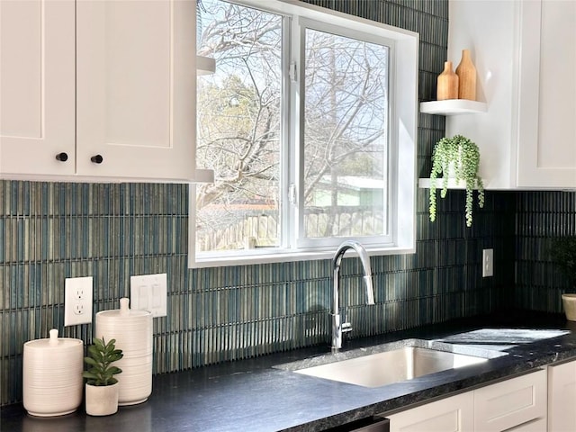 kitchen featuring dark countertops, white cabinets, backsplash, and a sink