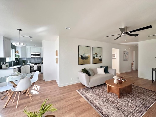 living room featuring a ceiling fan, baseboards, visible vents, and light wood finished floors