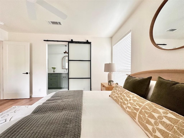 bedroom with a barn door, wood finished floors, visible vents, and connected bathroom