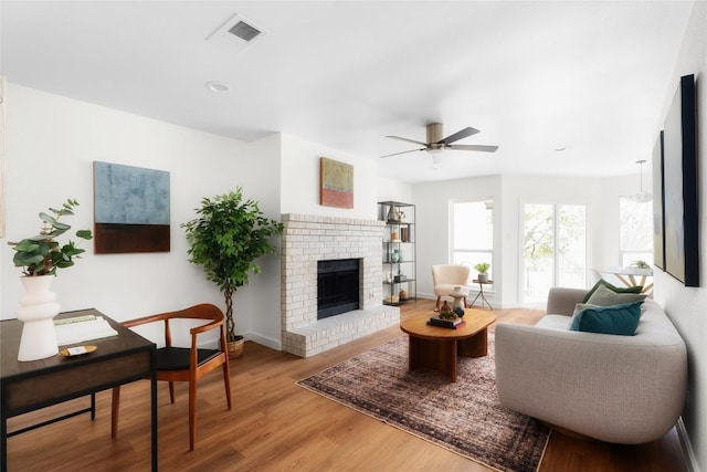 living room with visible vents, a brick fireplace, ceiling fan, baseboards, and wood finished floors