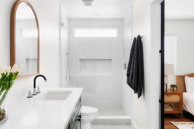 ensuite bathroom with visible vents, tiled shower, toilet, and vanity