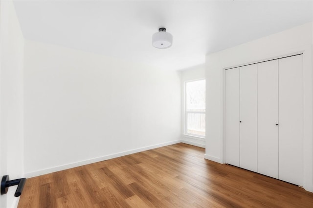 unfurnished bedroom with a closet, baseboards, and light wood-style floors