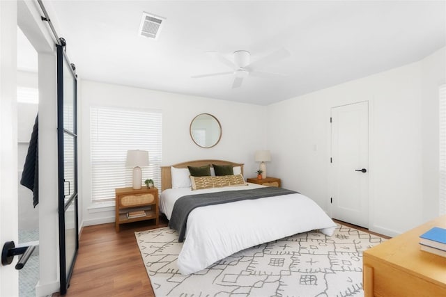 bedroom featuring baseboards, visible vents, light wood-style flooring, ceiling fan, and a barn door