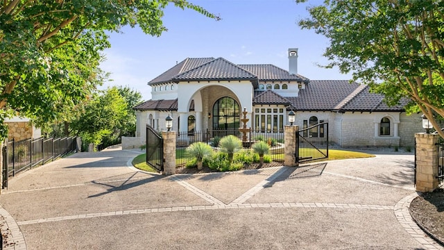 mediterranean / spanish house featuring a gate, a tile roof, a chimney, and fence