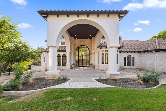 back of house featuring a tiled roof, a lawn, stone siding, and stucco siding