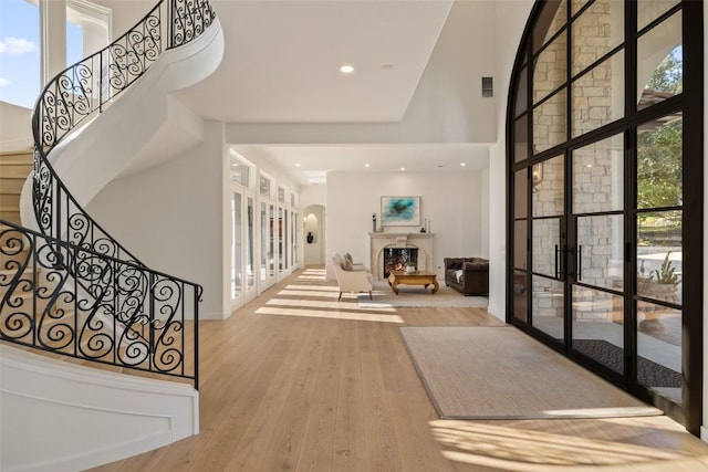 foyer entrance featuring a towering ceiling, hardwood / wood-style flooring, a warm lit fireplace, and stairway