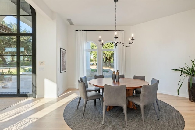 dining space with light wood-type flooring, baseboards, visible vents, and a notable chandelier