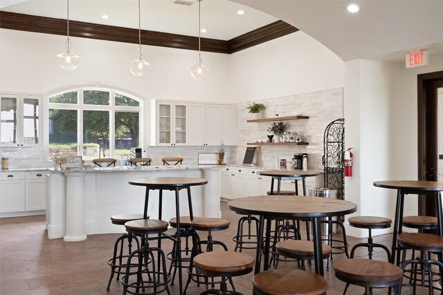 kitchen featuring a center island, white cabinets, backsplash, a high ceiling, and ornamental molding