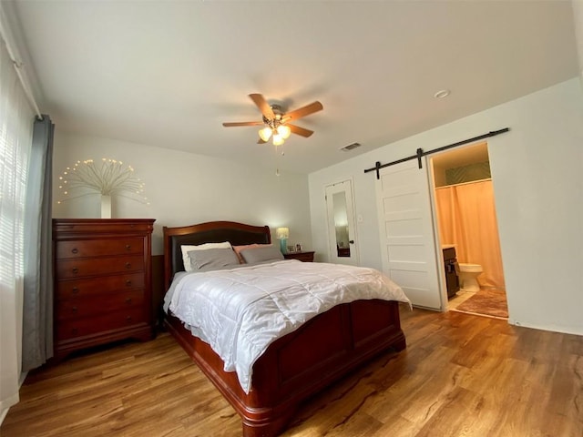 bedroom featuring ensuite bath, a barn door, visible vents, and wood finished floors