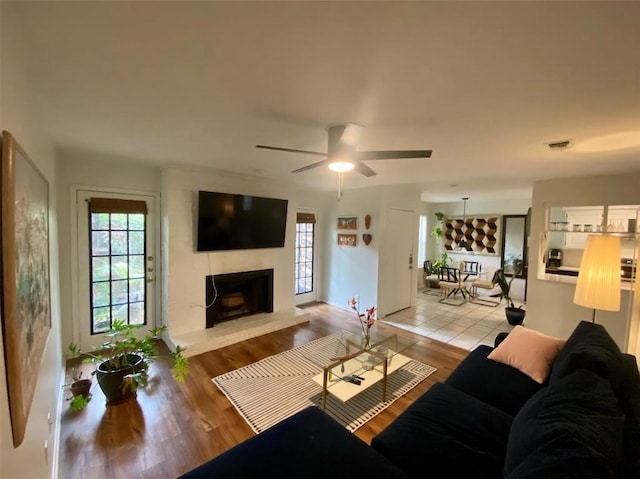 living room featuring a large fireplace, visible vents, ceiling fan, and wood finished floors