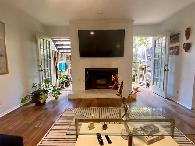 living area featuring a large fireplace, baseboards, and wood finished floors