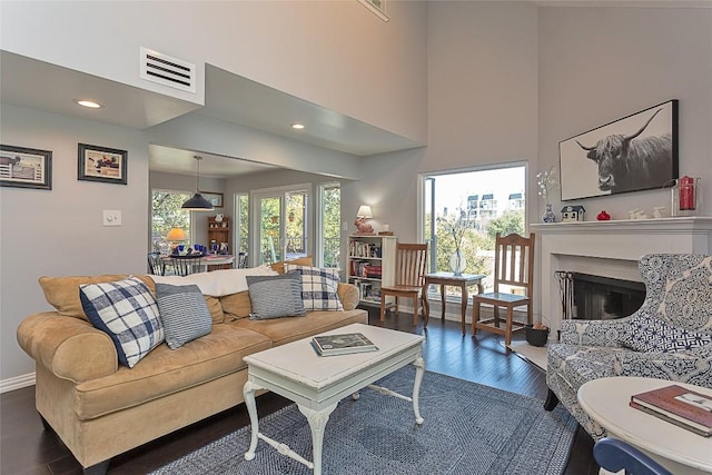 living area featuring visible vents, a healthy amount of sunlight, a fireplace, and dark wood-style flooring