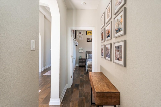 hallway featuring arched walkways, dark wood finished floors, and baseboards