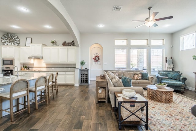 living room with dark wood-style floors, arched walkways, visible vents, ceiling fan, and baseboards