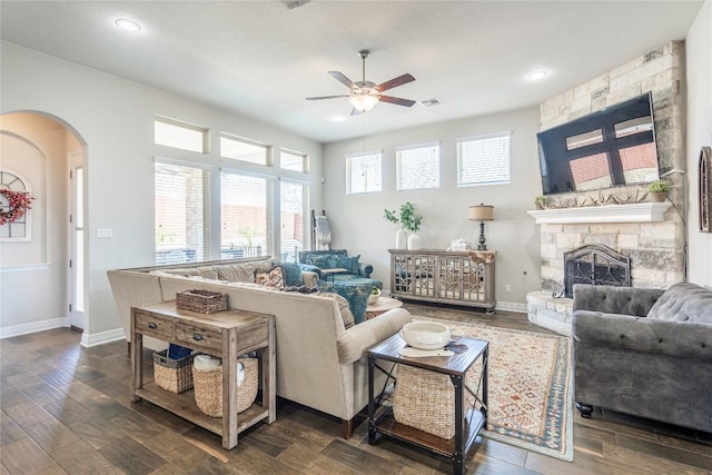 living area with arched walkways, a stone fireplace, dark wood-style flooring, and baseboards