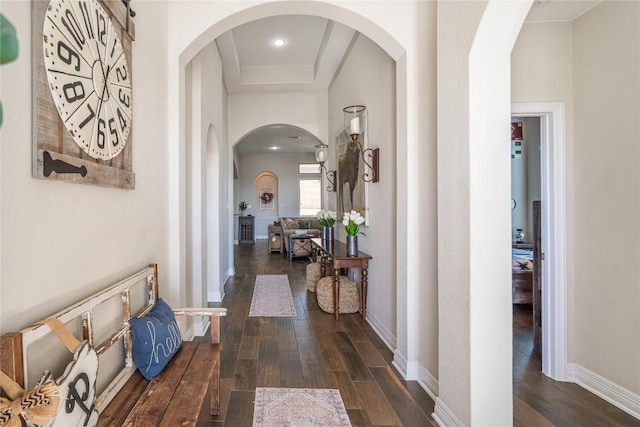 corridor with arched walkways, dark wood-style flooring, and baseboards