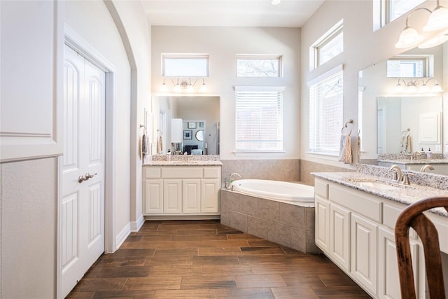 bathroom featuring a bath, two vanities, a sink, and wood finished floors